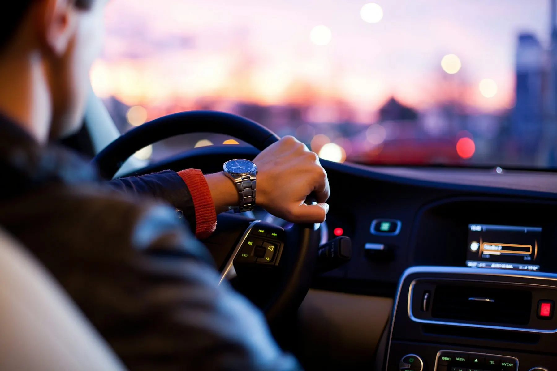 A driver’s hand on the steering wheel at sunset