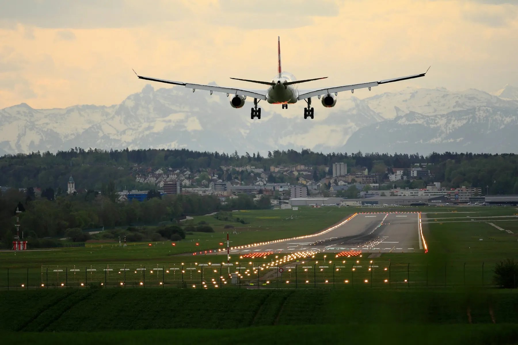 A passenger plane coming in to land over a lit runway at dusk